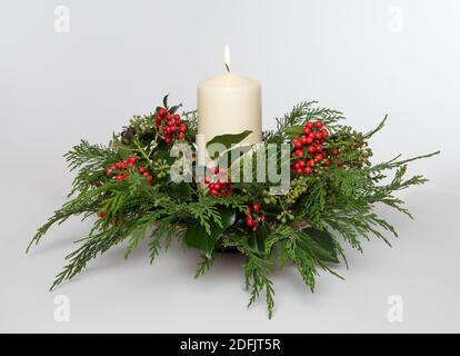 Isolato casa fatto festa natale tavolo decorazione con acini Holly, Fir, Ivy e una candela illuminata su uno sfondo semplice. Foto Stock