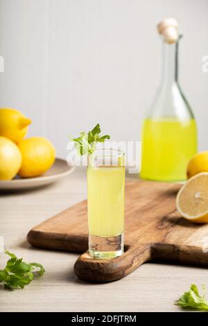 Liquore tradizionale italiano Limoncello. Bottiglia di vetro con liquore fatto in casa al limoncello, piatto con limoni e sedano. Foto Stock