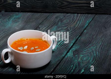 Zuppa di crema di pomodoro di zucca. Con l'aggiunta di semi di zucca. Su tavole di pino. Foto Stock
