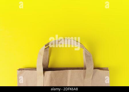 Primo piano di sacchetto di carta su sfondo giallo con spazio per la copia. Foto in posa piatta di borsa vuota per la spesa. Concetto di vendita estiva Foto Stock