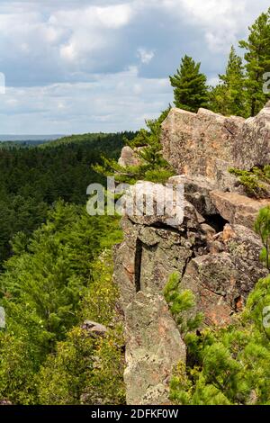 Una grande scogliera si erge sopra una foresta con colline che proseguono in lontananza. Gli alberi Evergreen appaiono in cima alle rocce della scogliera, vista dal lato. Foto Stock
