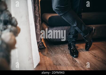 Una persona che indossa un paio di Oxford nero getto lucido scarpe e piedi con gambe incrociate Foto Stock