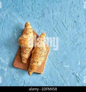 Due croissant freschi, tagliere in legno su sfondo blu. Vista dall'alto, spazio di copia Foto Stock