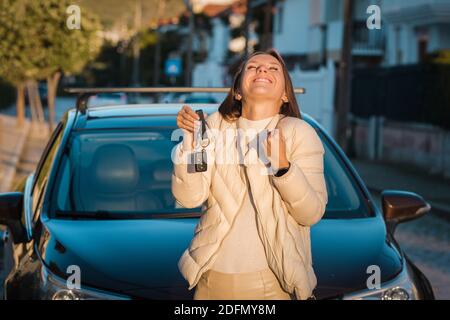 Felice attraente donna che tiene una chiave della sua nuova auto. Acquisto o noleggio auto di successo. Foto Stock