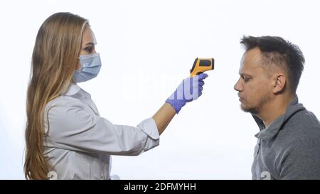 Test della temperatura corporea di un dipendente o di un paziente utilizzando un termometro senza contatto che indossa una maschera medica. Uomo triste infelice di malattia. Isolato su Foto Stock