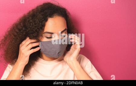 Giovane donna afroamericana in leggera t-shirt di peachy indossare una maschera riutilizzabile per evitare che altre persone possano contrarre l'infezione da corona COVID-19 e SARS COV 2 Foto Stock