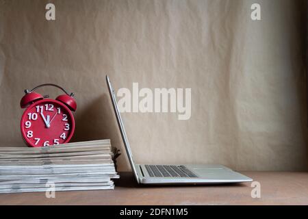 Orologio, giornali impilati e computer portatile sulla scrivania, straordinario lavoro concetto. Foto Stock