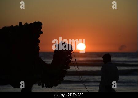 Pechino, Cina. 4 Dicembre 2020. Foto scattata il 4 dicembre 2020 mostra la silhouette di un cammello e del suo proprietario in attesa di clienti in spiaggia durante il tramonto nella città portuale pakistana meridionale di Karachi. Credit: Ahmad Kamal/Xinhua/Alamy Live News Foto Stock