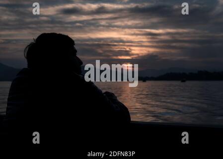 Silhouette di un uomo che guarda il tramonto su un lago Foto Stock