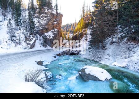 Il flusso di un bel fiume blu vicino a una strada di montagna in pineta. Paesaggio invernale. Foto Stock