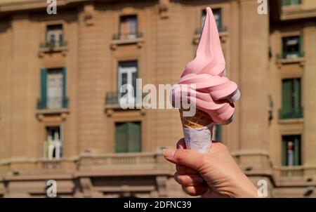 Mano della donna che tiene il delectable pastello Rosa Soft servire gelato Cono contro gli edifici d'epoca Foto Stock