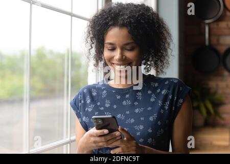 Sorridente donna di etnia africana millenaria che usa applicazioni mobili. Foto Stock