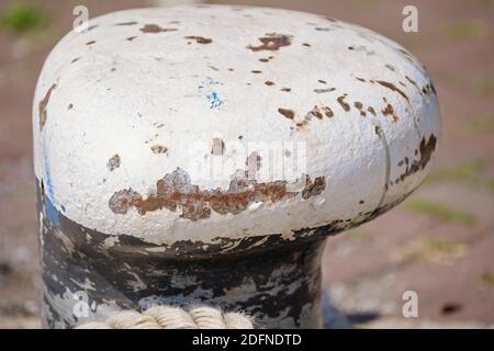 Astratto struttura di sfondo di bianco ruggine bollard. Una corda spessa e robusta si trova sul pavimento accanto al tollard. Foto Stock