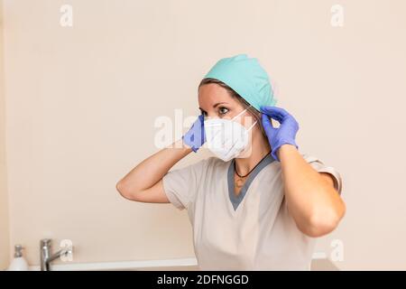 La ragazza dell'operatrice sanitaria è vestita con uniforme protettiva, cappuccio chirurgico, guanti in lattice e maschera Foto Stock