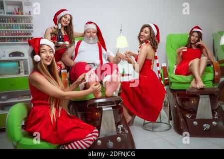 Bel Babbo Natale aiutanti fare manicure e pedicure a Babbo Natale in un salone termale Foto Stock