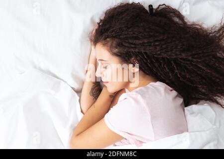 Primo piano vista dall'alto di una bella donna afro che dorme su lenzuola bianche di neve che giacciono sul grande letto. CopySpace. Foto Stock