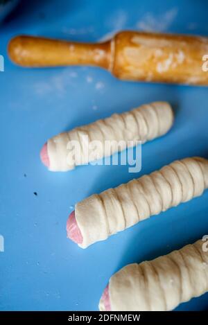 Sbozzati per torte fritte. Le salsicce sono avvolte in sottili strisce di impasto di lievito. L'impasto si sta alzando. Spazio di copia, messa a fuoco selettiva Foto Stock