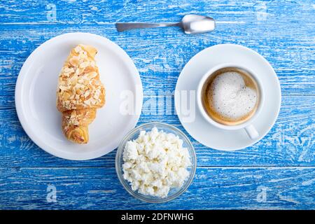 Colazione del mattino. Croissant francese fresco con caffè e formaggio casolare su una superficie di legno blu. Tradizioni culinarie francesi. Foto Stock