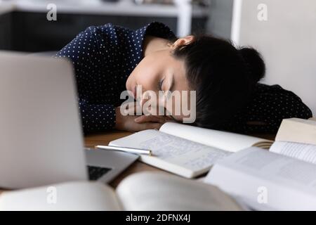 Donna di razza mista affaticata che dorme sul posto di lavoro tra i libri Foto Stock