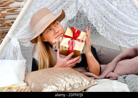 Donna di mezza età con cappello elegante che posa tra le scatole regalo di natale in una stanza decorata, concetto di Natale Foto Stock