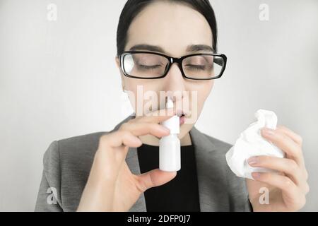 Giovane donna in occhiali, usa spray nasale. Foto Stock