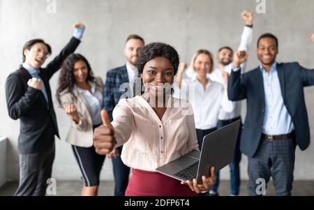 African Businesswoman gesturing Thumbs-Up in piedi con i colleghi in ufficio Foto Stock