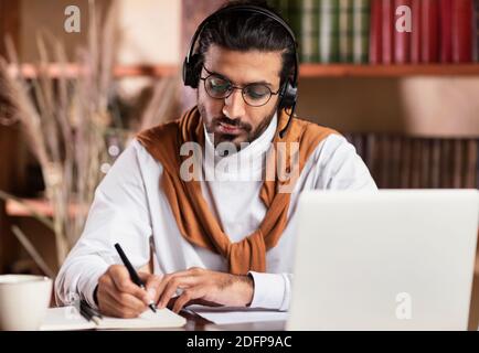 Indian Guy prendere appunti di apprendimento su laptop online a casa Foto Stock