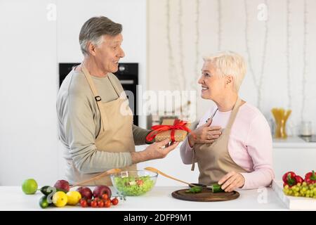 Marito anziano che dà il regalo alla moglie in cucina a casa Foto Stock