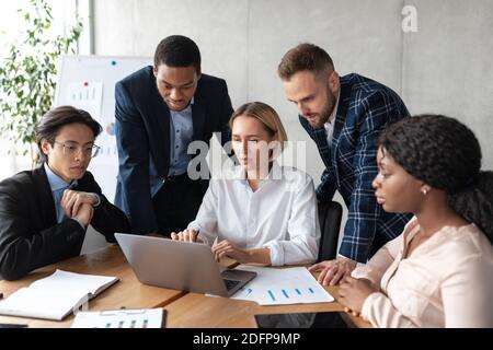 Team aziendale multietnico che lavora insieme su notebook seduti in ufficio Foto Stock