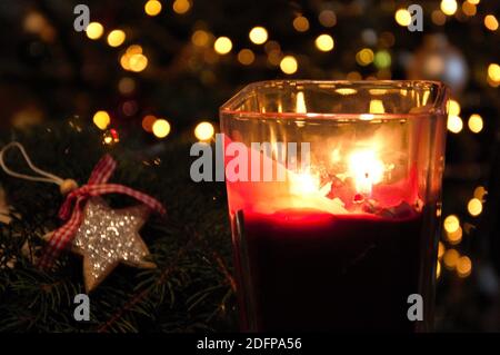 fiamme in contenitore di vetro rosso e una stella a forma di legno Decorazione di Natale da parte e luci offuscate sull'albero di Natale dentro sfondo nell'interno domestico Foto Stock