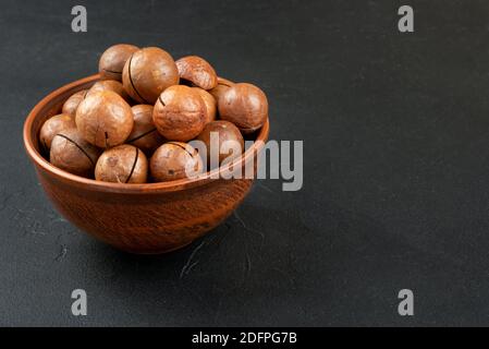 Noci di macadamia in una conchiglia e ciotola su un buio sfondo Foto Stock