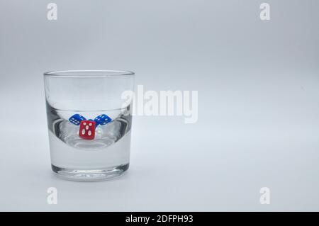 Bicchiere di alcol contenente dadi rossi e blu su bianco sfondo Foto Stock