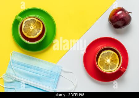 Tè con fette di limone al mattino. Festa del tè per due e frutta di mela. Due mascherine protettive sul tavolo nel caffè. Due tazze con rosso e gre Foto Stock