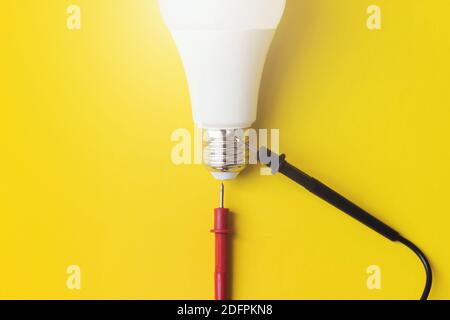 Concetto di energia vitale. Lampadina con sonde del multimetro su sfondo giallo. Concetto di tecnologia. Vista dall'alto, disposizione piatta Foto Stock