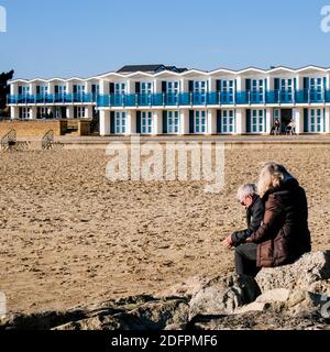 Poole Dorset UK, dicembre 06 2020, Senior Man and Woman Couple seduta su Rocks at the Beach rilassante sotto il cielo Azzurro Foto Stock