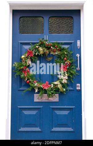 Corona dell'Avvento compostabile con foglie sempreverdi, nastri rossi e dorati e canne caramelle. Corona appesa su una casa blu porta di fronte a Highgate, Londra. Foto Stock