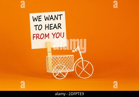 Stendibiancheria in legno con foglio di carta bianco. Testo 'vogliamo sentire da voi'. Modello di bicicletta in miniatura. Bellissimo sfondo arancione. Business e suppo Foto Stock