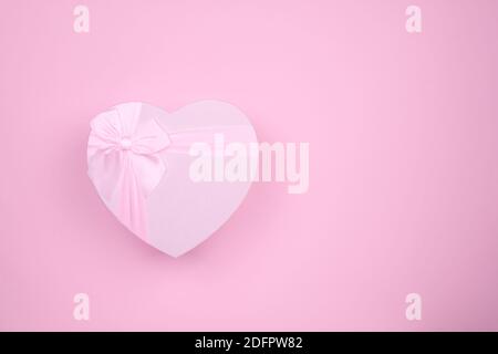 Regalo rosa a forma di cuore con arco per San Valentino su sfondo rosa, minimalismo. Foto Stock