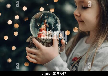 Ragazza che guarda una palla di vetro con una scena di La nascita di Gesù Cristo in una palla di vetro Foto Stock