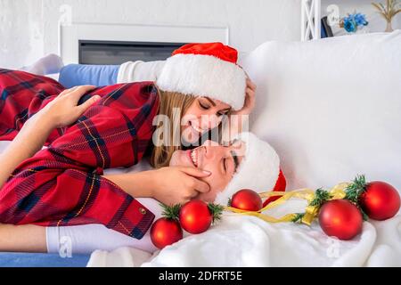 Ritratto di un uomo e di una donna con vista laterale sdraiati Un divano circondato da palle di Natale che indossano cappelli santa e. pigiami Foto Stock