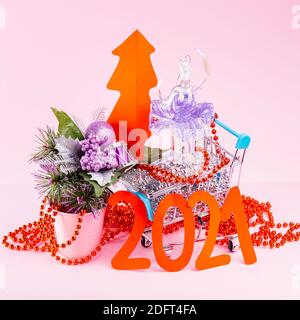 Albero di Natale rosso e l'iscrizione 2021 nel carrello. Decorazioni dell'albero di Natale nel carrello della spesa su sfondo rosa. Concetto di vacanza Foto Stock