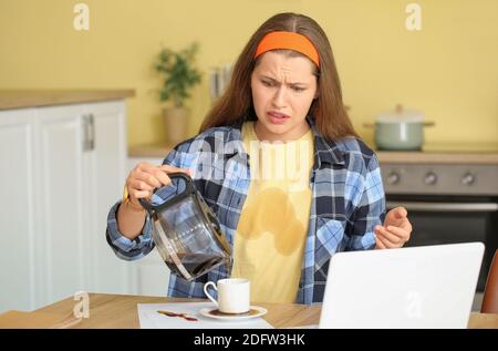 Giovane donna stressata con macchie di caffè sulla sua t-shirt e. caffè versato in cucina Foto Stock