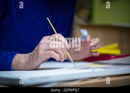 Imparare nuovi hobby durante la quarantena e il blocco di Coronavirus. Donna anziana artista dipinge a casa. Attraente vecchia donna disegna e fa il suo favore Foto Stock