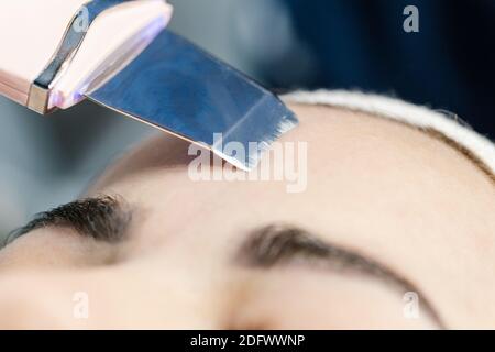 Primo piano la procedura di peeling viso ultrasonico nei saloni di bellezza. Il dispositivo per la pulizia del viso a ultrasuoni. Cosmetologia hardware. Foto Stock