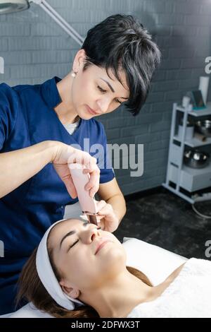 Donna che riceve la terapia di pulizia con un'apparecchiatura ultrasonica professionale da medico-cosmetologo in ufficio di cosmetologia. Cosmetologia e professionale Foto Stock