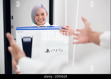 La ragazza ha appena ottenuto un delirio di una nuova PlayStation 5 console di gioco e sorprendente il suo ragazzo con un regalo a. gioca insieme su un autoisolamento Foto Stock