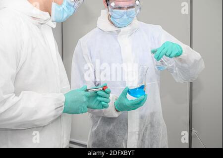 Coppia scienziato maschile indossando tuta di protezione contenente il vaccino e lavorando con molte attrezzature di laboratorio per la ricerca di vaccino in laboratorio. Ricerca medica Foto Stock