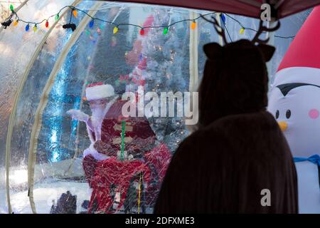 Seattle, Washington, Stati Uniti. 6 dicembre 2020. L'assistente LaRae Weidner guarda a Dan Kemmis, conosciuto come Seattle Santa, accoglie i visitatori da una bolla protettiva di plastica nel quartiere Greenwood di Seattle. Incapace di programmare eventi privati a causa della pandemia del coronavirus, Kemmis sta facendo apparizioni pubbliche fisicamente distanziate con alcune donazioni che avvantaggiano i rifugi locali dei senzatetto. Credit: Paul Christian Gordon/Alamy Live News Foto Stock