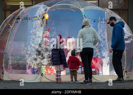 Seattle, Washington, Stati Uniti. 6 dicembre 2020. DaN Kemmis, noto come Seattle Santa, saluta una giovane famiglia da una bolla protettiva di plastica nel quartiere Greenwood di Seattle. Incapace di programmare eventi privati a causa della pandemia del coronavirus, Kemmis sta facendo apparizioni pubbliche fisicamente distanziate con alcune donazioni che avvantaggiano i rifugi locali dei senzatetto. Credit: Paul Christian Gordon/Alamy Live News Foto Stock