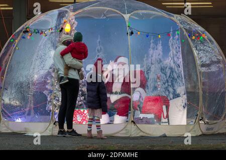 Seattle, Washington, Stati Uniti. 6 dicembre 2020. DaN Kemmis, noto come Seattle Santa, saluta una giovane famiglia da una bolla protettiva di plastica nel quartiere Greenwood di Seattle. Incapace di programmare eventi privati a causa della pandemia del coronavirus, Kemmis sta facendo apparizioni pubbliche fisicamente distanziate con alcune donazioni che avvantaggiano i rifugi locali dei senzatetto. Credit: Paul Christian Gordon/Alamy Live News Foto Stock